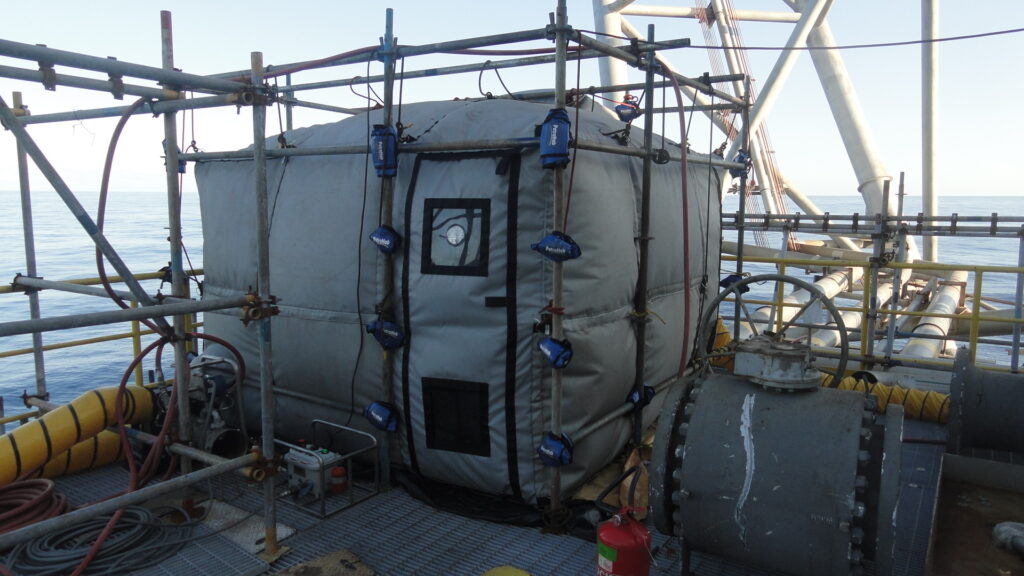 A large industrial insulated pipe joint with scaffolding and safety equipment.