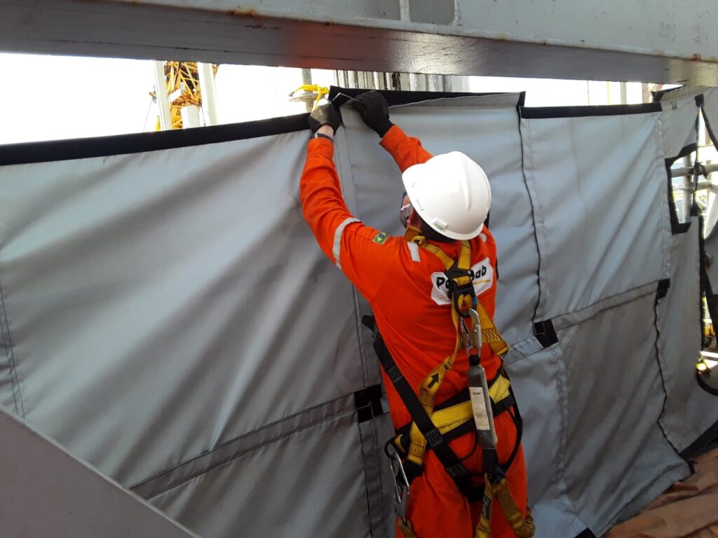 Worker in safety gear securing a tarp or barrier indoors.